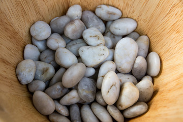 Fototapeta na wymiar White river pebble stones on a wooden bowl. Bunch of rocks for decorating interiors. Concept: Holding them together.