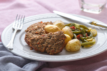 Meatloaf dinner on a pink table cloth with knife and fork