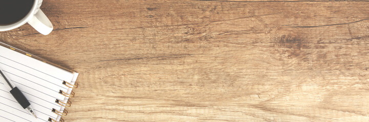 Panoramic top view on a wooden empty desk with open notebook and coffee cup
