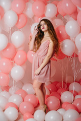 Beautiful young girl in a dress among a lot of pink balls.