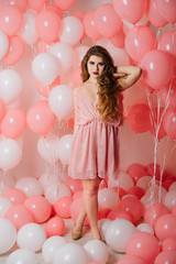 Beautiful young girl in a dress among a lot of pink balls.