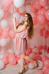 Beautiful young girl in a dress among a lot of pink balls.