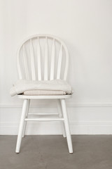 White old-fashioned retro style chair standing in an empty room in front of a wall on light parquet floor. Natural light from the window