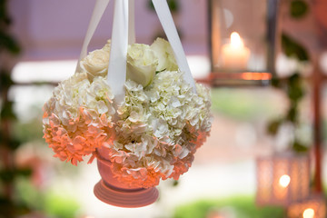 Beautiful flower bouquet hanging with candles in the background. Closeup of white flowers with blurred bokeh candlelights. Romantic concept.