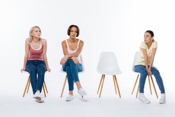 Obraz premium Special project. Serious nice young women sitting on the chair and waiting for their friend while participating in the social project