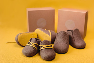 Brown, children's handmade shoes made of merino wool on a bright yellow background.