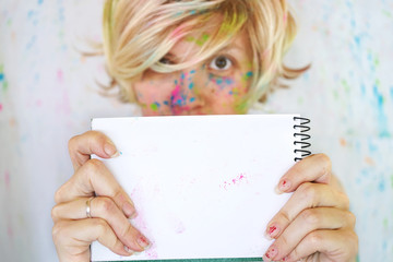Mujer joven con la cara llena de pintura sujetando un cuaderno en blanco 