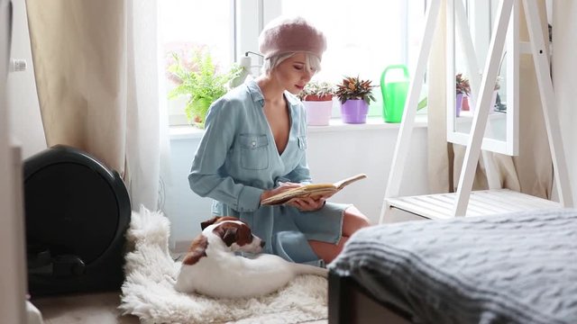 Young blonde girl with dog at home reading a book
