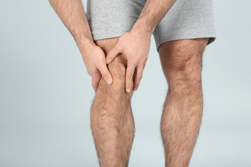 Young man suffering from knee pain on light background