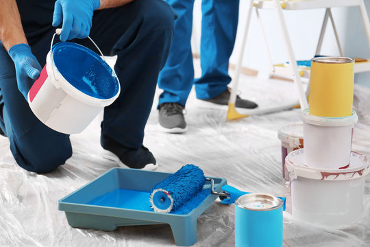 Male decorator pouring paint into tray indoors
