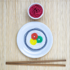 Strings in different colors in form of sushi roll and soy sauce with sticks on beige bamboo mat minimalistic abstract concept