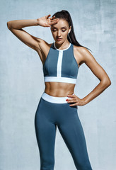 Fototapeta na wymiar Tired woman resting after doing sports. Photo of latin woman in fashionable sportswear on grey background. Strength and motivation