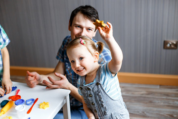 Picture of a father, daughter and son playing with color play dough and cutters. Having fun with colorful modeling clay. Creative kids molding at home. Children play with plasticine or dough.