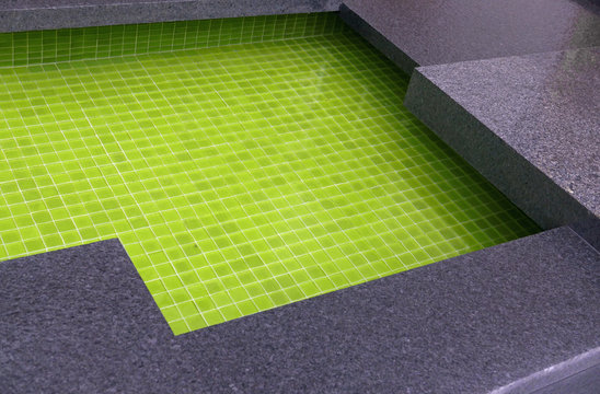Ausschnitt eines Wasserbeckens mit grünen Glaskacheln und rechteckiger Steinumrandung
