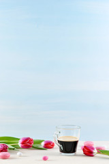 Pink tulips and pink macaroons. The composition is complemented by a transparent cup of coffee. Light background. Vertical orientation of the frame. Negative space.