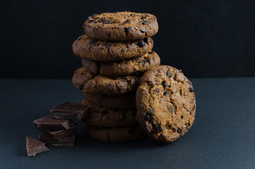 Chocolate chip cookies and chocolate pieces on dark background.