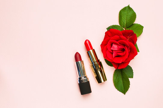 Red lipstick with red roses on pink background with copy space. Makeup Accessories Top view Flat Lay. Various cosmetic products for make-up.