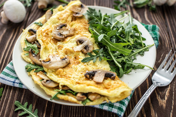 Omelette with mushrooms and arugula on a wooden background