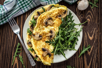 Omelette with mushrooms and arugula on a wooden background