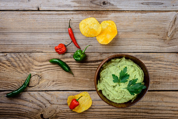 Obraz na płótnie Canvas Guacamole in a wood bowl with chips and fresh ingredients on a rustic wooden background, top view