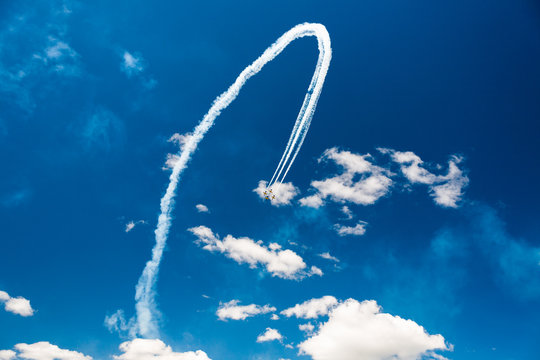A group of professional pilots of military aircraft of fighters on a sunny clear day shows tricks in the blue sky, leaving beautiful traces of clouds scattered in different directions.