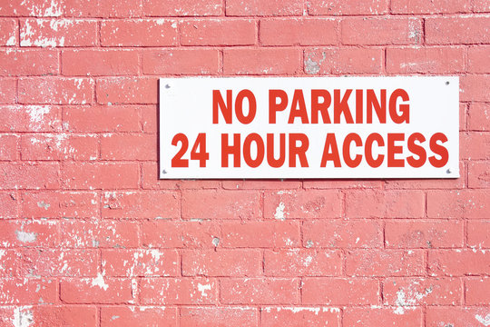 No parking 24 hr hour access required sign on red brick wall