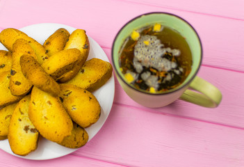Rusks on a white plate and a cup of tea on a wooden pink background.