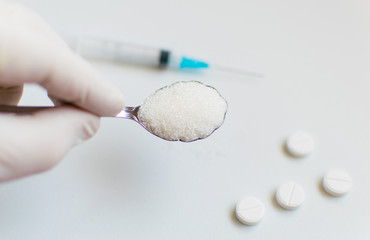 Obraz na płótnie Canvas A spoon of sugar, a syringe and pills on a white background. The concept of harm to sugar and the onset of diabetes.