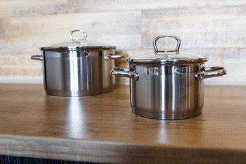 Image of kitchen ware. Set of shiny stainless steel saucepans big and small on wooden surface