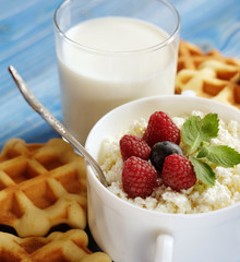 Cottage cheese with berries, waffles and milk on a wooden blue background. Close up.