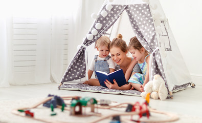 family mother reading to children book in tent at home.