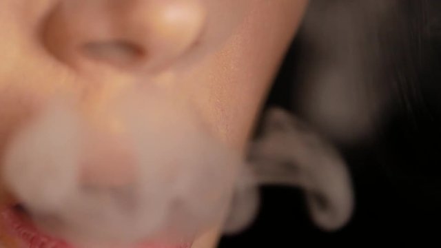 Close up of woman mouth smoking. The girl slowly and sexually releases smoke from an electronic cigarette