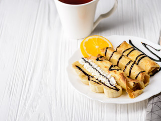 Pancakes with banana, whipped cream decorated with chocolate syrup on white wooden background. And a cup of tea
