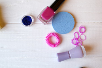 Naklejka premium Colorful and bright cosmetics. Beauty care tools. Beauty salon. Girl's paradise. Nail polishes, sequins, pink hair bands and comb on the white wooden desk. Bright still life of beauty instruments.