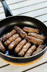 Cevapcici, skinless sausages from the Balkans made of minced pork, beef or lamp meat grilled in pan on wooden table