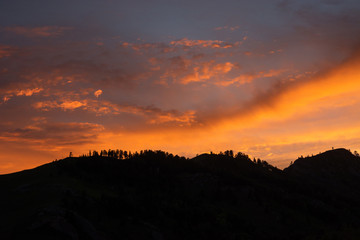 Silhouettes of mountains in beautiful sunset sky. Forest on top of mountain.