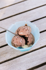 Sundae with scoops of vanilla and chocolate ice cream served in blue plastic cup with stainless steel spoon on wooden garden table