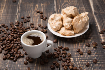 a cup of coffee and meringue on a saucer on old wooden boards, coffee beans scattered