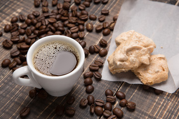 a cup of coffee and meringue on parchment paper on old wooden boards, coffee beans scattered