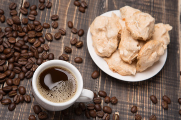 a cup of coffee and meringue on a saucer on old wooden boards, coffee beans scattered