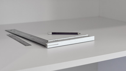 Two metal rulers and pencil lying on white wooden shelf