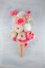 Flatlay waffle sweet ice cream cone with pink tulips and roses blossom flowers over white wood background, top view. Spring or summer mood concept.