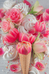 Flatlay waffle sweet ice cream cone with pink tulips and roses blossom flowers over white wood background, top view. Spring or summer mood concept.
