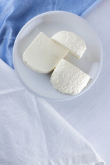 Cheese, cheese on a white plate, a glass of yogurt, minimalism, top view, copy space, dairy products on a white napkin, blue cloth, cheese pattern, French breakfast, white cheese on a white background