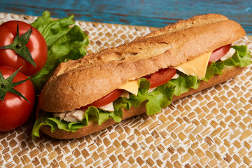 Fresh submarine sandwich with chicken fillet, cheese, fresh tomatoes, lettuce, cucumbers and onions on wooden background