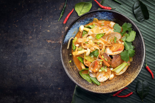 Traditional Thai kaeng phet red curry with clams and vegetable as top view in a bowl with copy space left