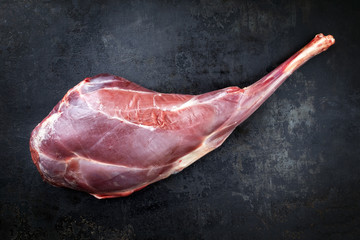 Raw aged leg of venison with bone as top view on rustic background - obrazy, fototapety, plakaty