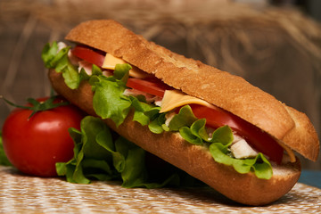 Fresh submarine sandwich with chicken fillet, cheese, fresh tomatoes, lettuce, cucumbers and onions on wooden background