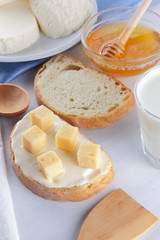 Cheese on a white plate, a glass of yogurt, a sandwich with soft cheese, minimalism, top view, copy space, a piece of bread with hard cheese, blue cloth, French breakfast, white cheese on a white back