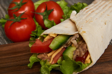 Burrito with grilled chicken and vegetables lettuce, fresh tomatoes, cucumber, onion and cheese rolled in pita bread on wooden background, close-up